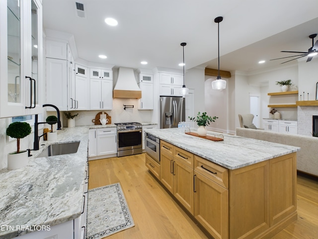 kitchen featuring custom range hood, appliances with stainless steel finishes, light wood-style floors, open floor plan, and a sink