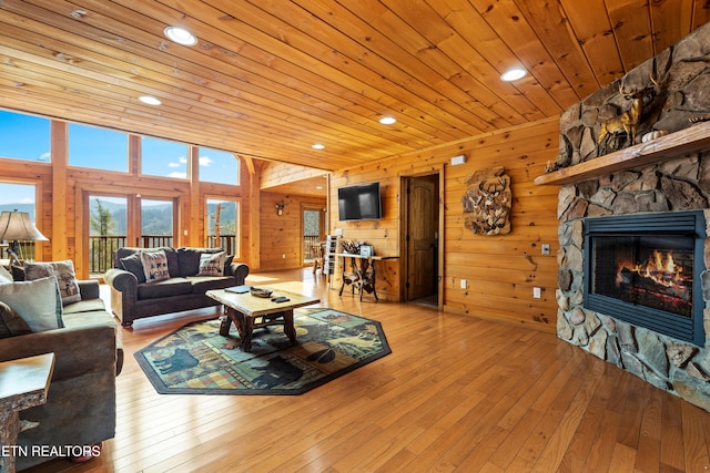 living room with light hardwood / wood-style floors, a stone fireplace, wooden ceiling, and wood walls