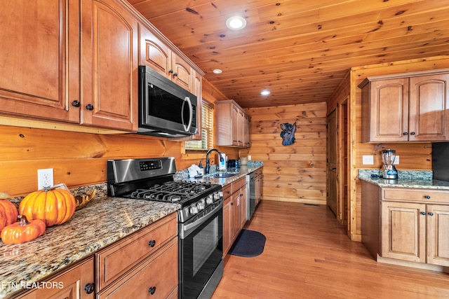 kitchen with sink, wooden walls, light hardwood / wood-style flooring, dark stone countertops, and stainless steel appliances