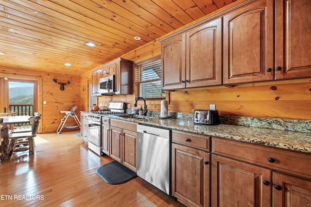 kitchen featuring stone counters, wooden walls, light wood-type flooring, and appliances with stainless steel finishes