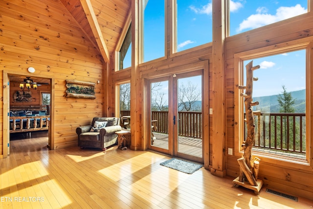 interior space featuring french doors, wooden walls, high vaulted ceiling, beamed ceiling, and light hardwood / wood-style floors