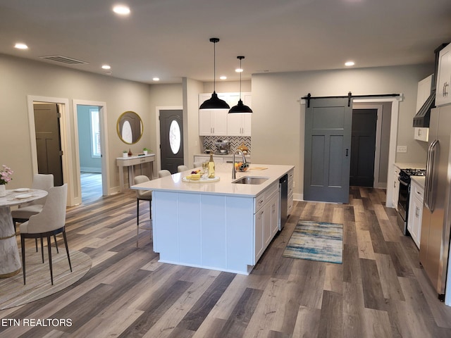 kitchen featuring sink, stainless steel appliances, a barn door, a center island with sink, and white cabinets