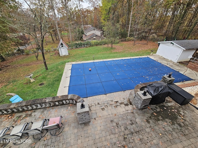 view of swimming pool with a lawn, a storage unit, and a patio