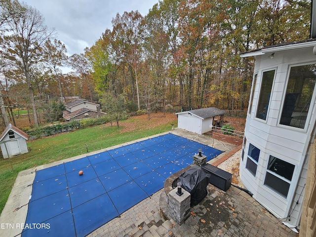 view of swimming pool featuring a lawn, a patio, and a shed