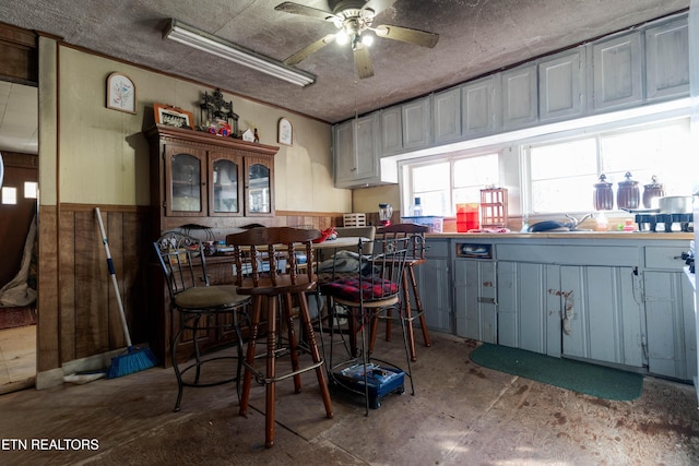 kitchen with wood walls, crown molding, ceiling fan, and concrete floors