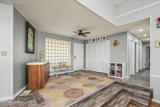 foyer with a textured ceiling, ceiling fan, and wood walls