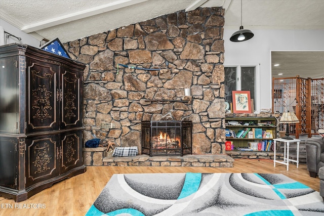 living room featuring hardwood / wood-style floors, lofted ceiling with beams, a stone fireplace, ornamental molding, and a textured ceiling