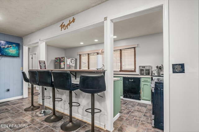 kitchen with a textured ceiling, wood walls, a breakfast bar area, and green cabinetry