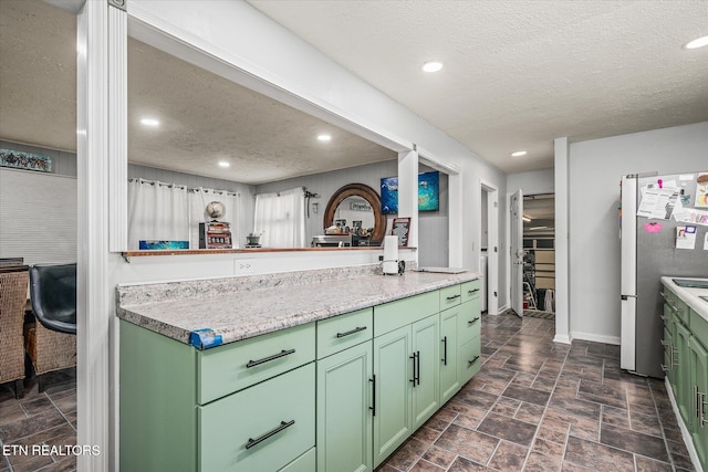 kitchen with stainless steel fridge, a textured ceiling, and green cabinetry