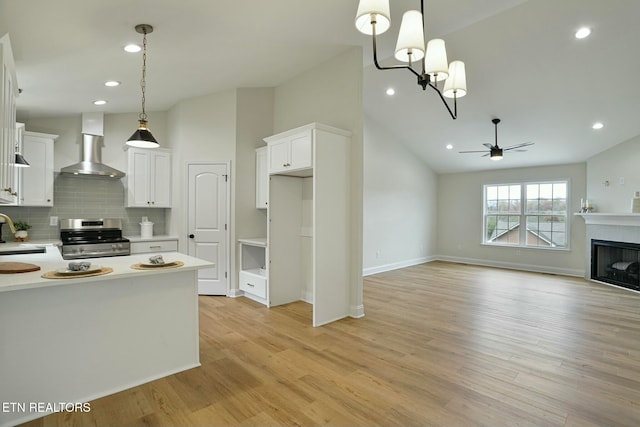 kitchen featuring wall chimney exhaust hood, stainless steel range oven, sink, hanging light fixtures, and white cabinets