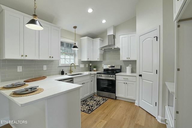 kitchen with stainless steel electric range, sink, white cabinets, hanging light fixtures, and wall chimney exhaust hood