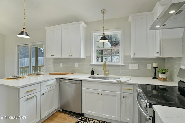 kitchen featuring pendant lighting, sink, wall chimney range hood, appliances with stainless steel finishes, and white cabinets