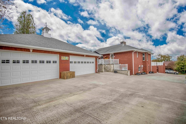 view of side of property with a garage, concrete driveway, brick siding, and a chimney