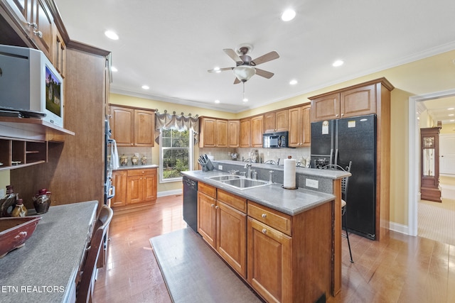 kitchen with tasteful backsplash, light hardwood / wood-style floors, a center island with sink, black appliances, and ornamental molding