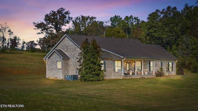 back house at dusk featuring central AC unit, covered porch, and a yard