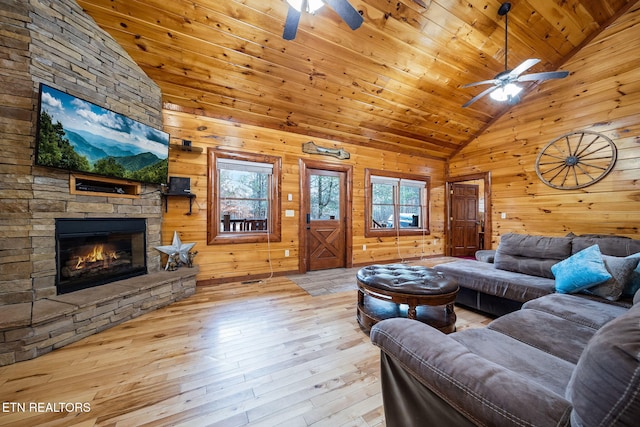 living room featuring wood walls, high vaulted ceiling, a stone fireplace, light hardwood / wood-style floors, and wood ceiling