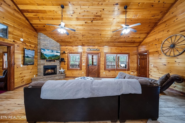 living room with wood ceiling, ceiling fan, high vaulted ceiling, a stone fireplace, and wood walls