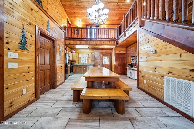 dining space with a towering ceiling, an inviting chandelier, wooden walls, and wood ceiling