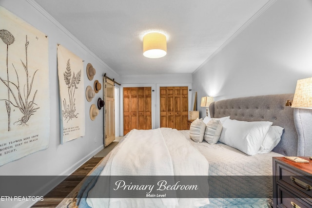 bedroom featuring a barn door, two closets, crown molding, and dark wood-type flooring