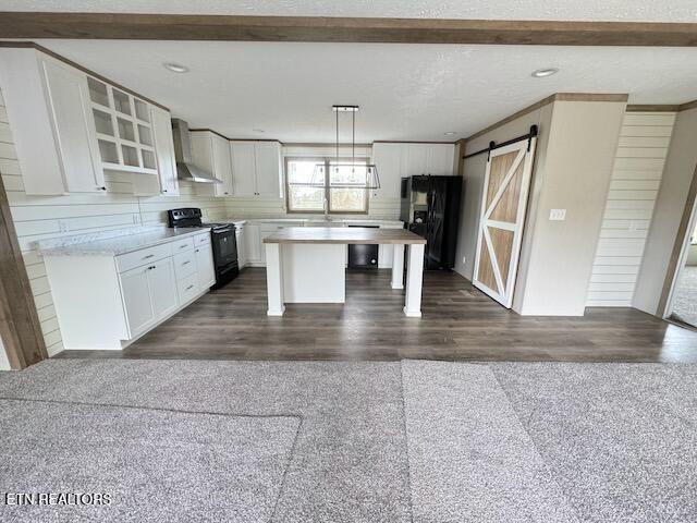 kitchen featuring a center island, wall chimney exhaust hood, hanging light fixtures, a barn door, and black appliances