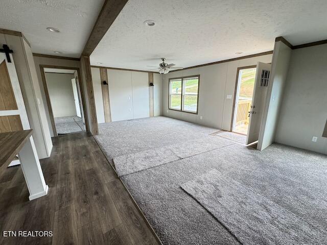 unfurnished living room with crown molding, ceiling fan, a barn door, a textured ceiling, and dark hardwood / wood-style flooring