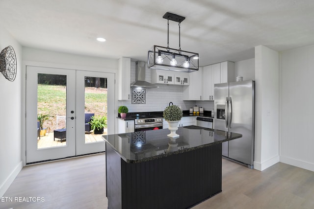 kitchen featuring french doors, stainless steel appliances, wall chimney range hood, white cabinets, and a center island