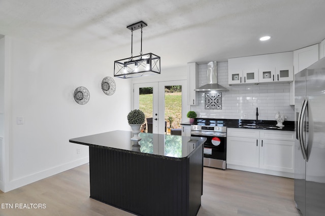 kitchen with wall chimney exhaust hood, stainless steel appliances, sink, white cabinets, and a center island