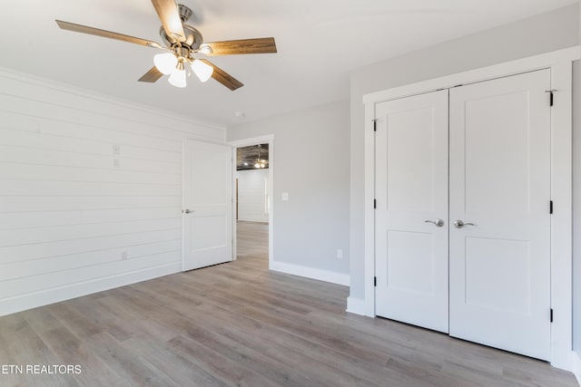 unfurnished bedroom with light hardwood / wood-style floors, a closet, ceiling fan, and wood walls