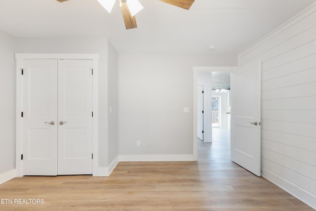 unfurnished bedroom featuring light hardwood / wood-style floors, a closet, ceiling fan, and wood walls