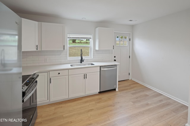 kitchen with backsplash, white cabinets, sink, light hardwood / wood-style flooring, and appliances with stainless steel finishes