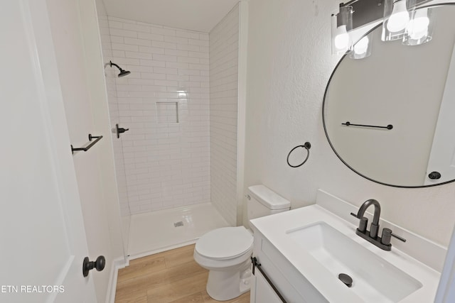 bathroom with toilet, wood-type flooring, vanity, and a tile shower