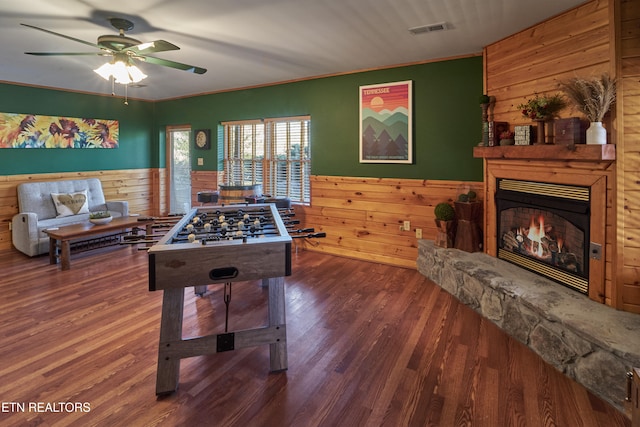 rec room featuring wooden walls, dark hardwood / wood-style floors, ceiling fan, ornamental molding, and a fireplace