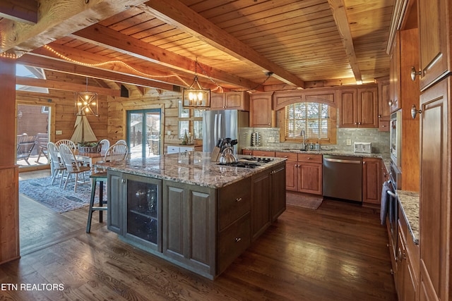 kitchen featuring a healthy amount of sunlight, dark wood-type flooring, stainless steel appliances, wooden walls, and a kitchen island with sink