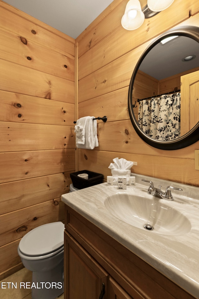 bathroom with wood walls, toilet, tile patterned floors, and vanity