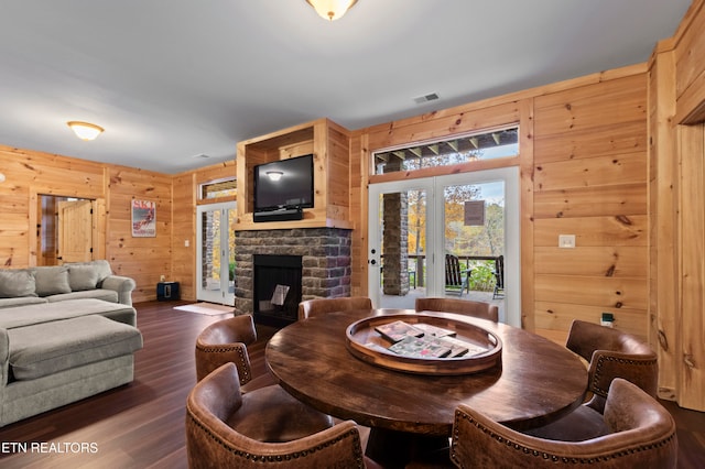 dining space featuring a fireplace, wooden walls, dark hardwood / wood-style floors, and french doors