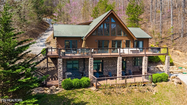 rear view of property with stone siding, stairs, a wooden deck, and a forest view