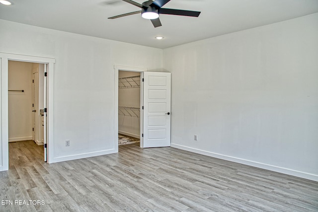 unfurnished bedroom featuring ceiling fan, a closet, a spacious closet, and light hardwood / wood-style flooring