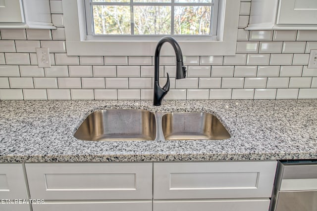 room details featuring white cabinets, backsplash, light stone countertops, and sink