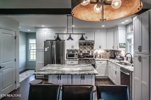 kitchen featuring light stone countertops, appliances with stainless steel finishes, sink, decorative light fixtures, and a kitchen island