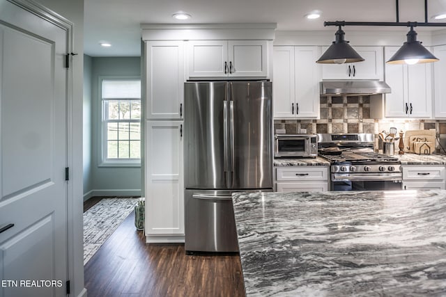 kitchen featuring appliances with stainless steel finishes, dark stone counters, dark wood-type flooring, decorative light fixtures, and white cabinets