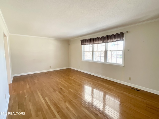 empty room with visible vents, wood-type flooring, baseboards, and ornamental molding