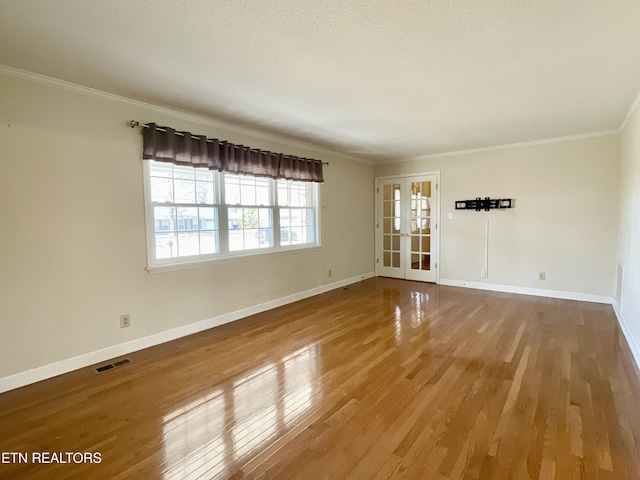 empty room with wood finished floors, visible vents, baseboards, french doors, and crown molding