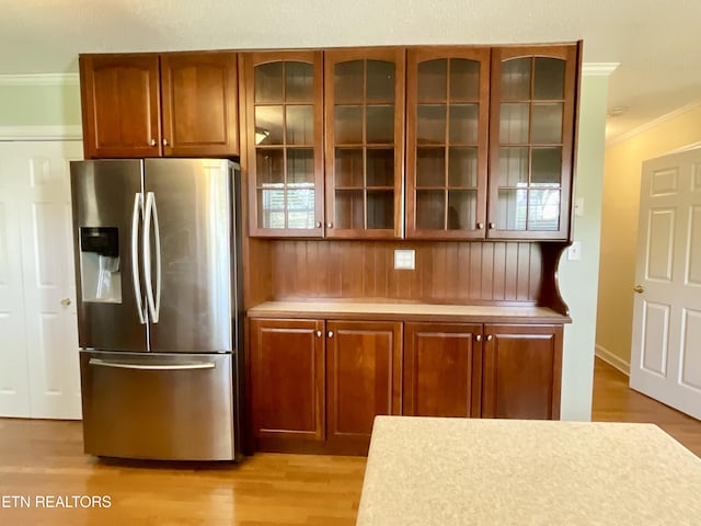 kitchen featuring light wood-style flooring, light countertops, glass insert cabinets, stainless steel refrigerator with ice dispenser, and crown molding