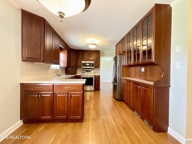 kitchen with light wood finished floors, a sink, stainless steel appliances, light countertops, and glass insert cabinets