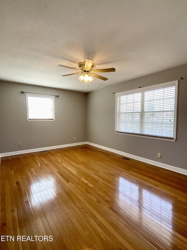 empty room featuring hardwood / wood-style floors, ceiling fan, baseboards, and a textured ceiling