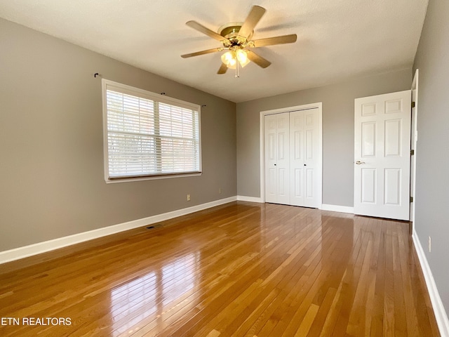 unfurnished bedroom featuring visible vents, baseboards, hardwood / wood-style floors, a closet, and a ceiling fan