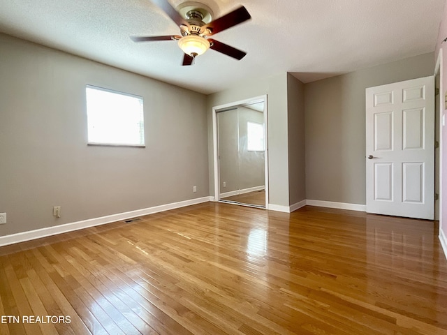 unfurnished bedroom featuring light wood-style flooring, multiple windows, baseboards, and a closet