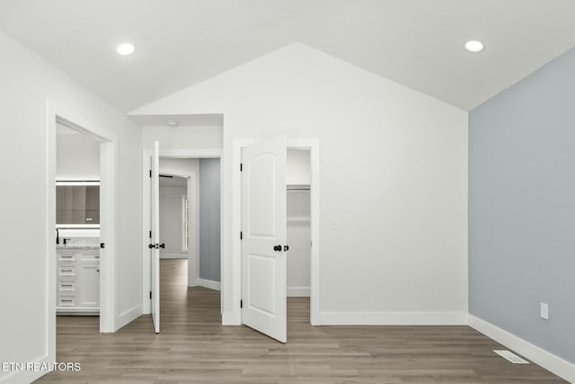 unfurnished bedroom featuring a closet, a walk in closet, light hardwood / wood-style flooring, and vaulted ceiling