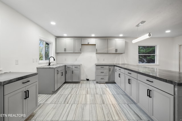 kitchen featuring kitchen peninsula, hanging light fixtures, gray cabinetry, and sink