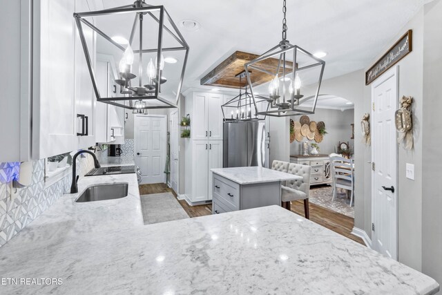 kitchen with sink, hanging light fixtures, a kitchen island, stainless steel fridge, and white cabinets